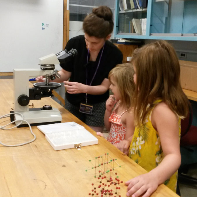 A conservator and two children having a look under the microscope