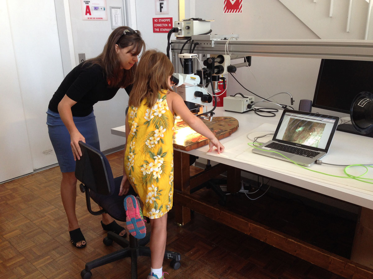 A conservator and a child looking at a panel painting under a microscope